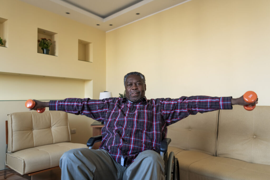 Senior man in Wheelchair who is Exercising with Dumbbells at Home in the Living Room.