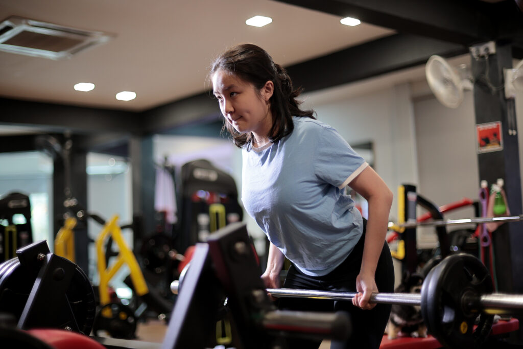 An Asian teenage girl is practicing weights for good posture in gym centre
