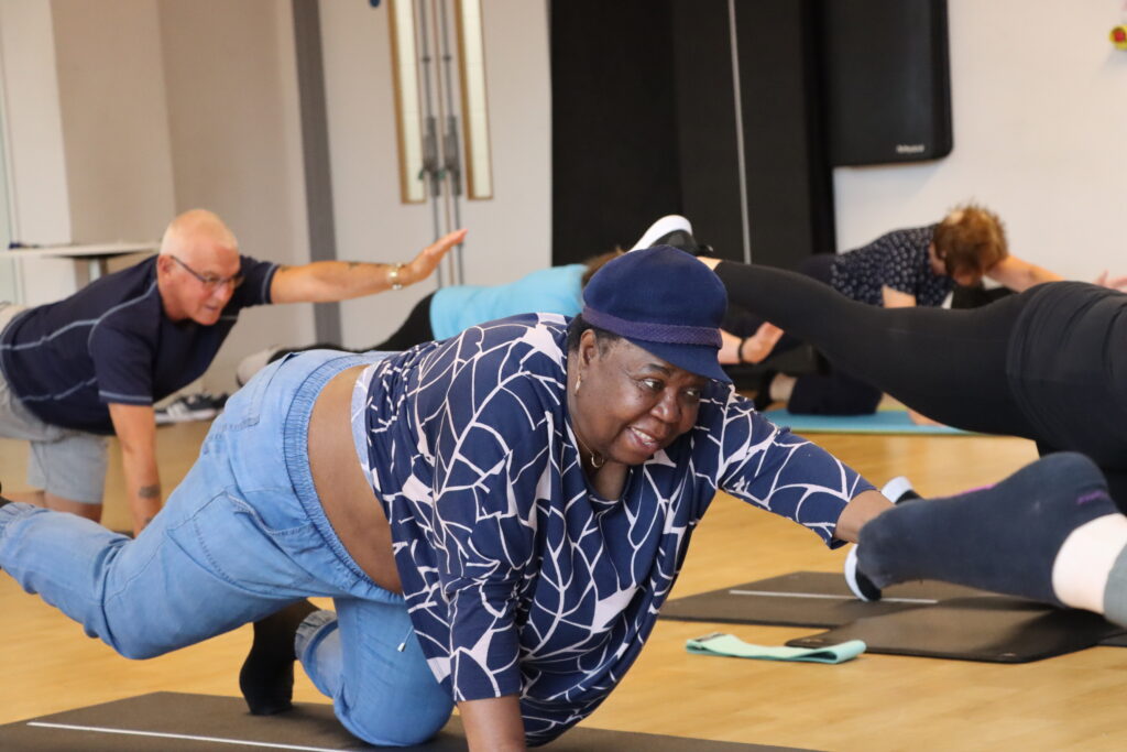 Woman exercising on floor with group of people inside fitness studio